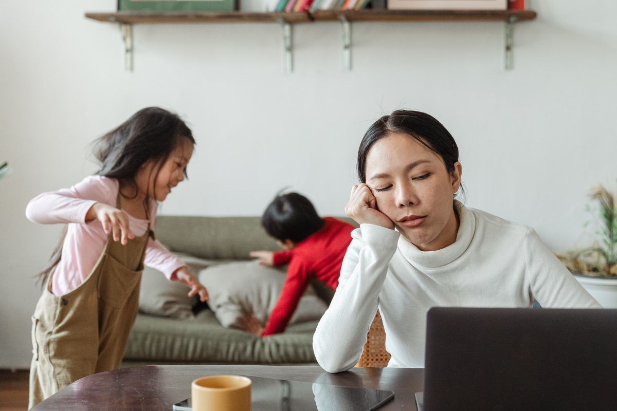 Mae trabalhando home office, seus filhos correndo pela casa