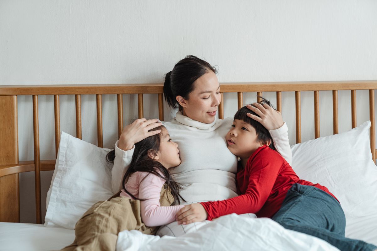 mÃE COM DOIS FILHOS DEITADA NA CAMA CONVERSANDO.